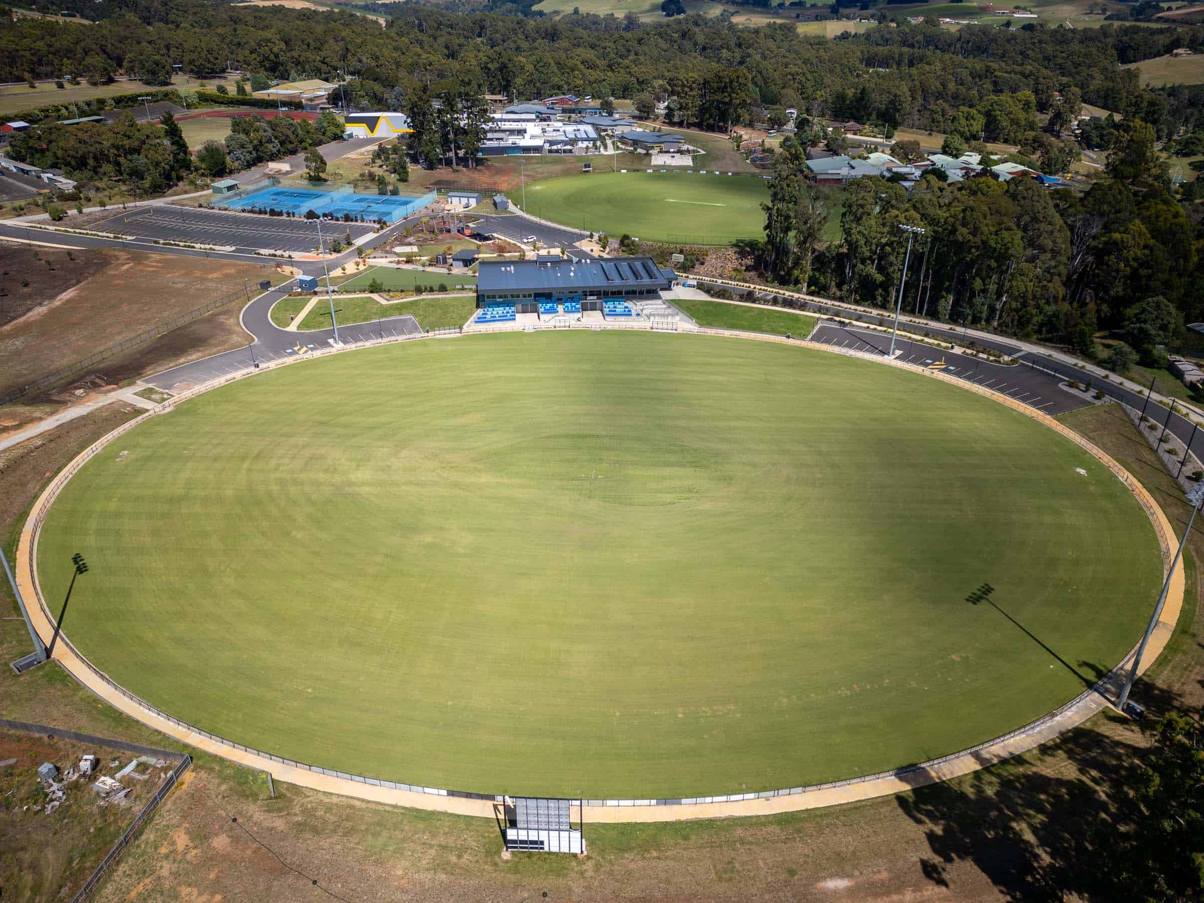 Aerial view of the main oval at Dial Park in Penguin, with grandstand, seating, lighting towers, car parks, and surrounding sports and school facilities.