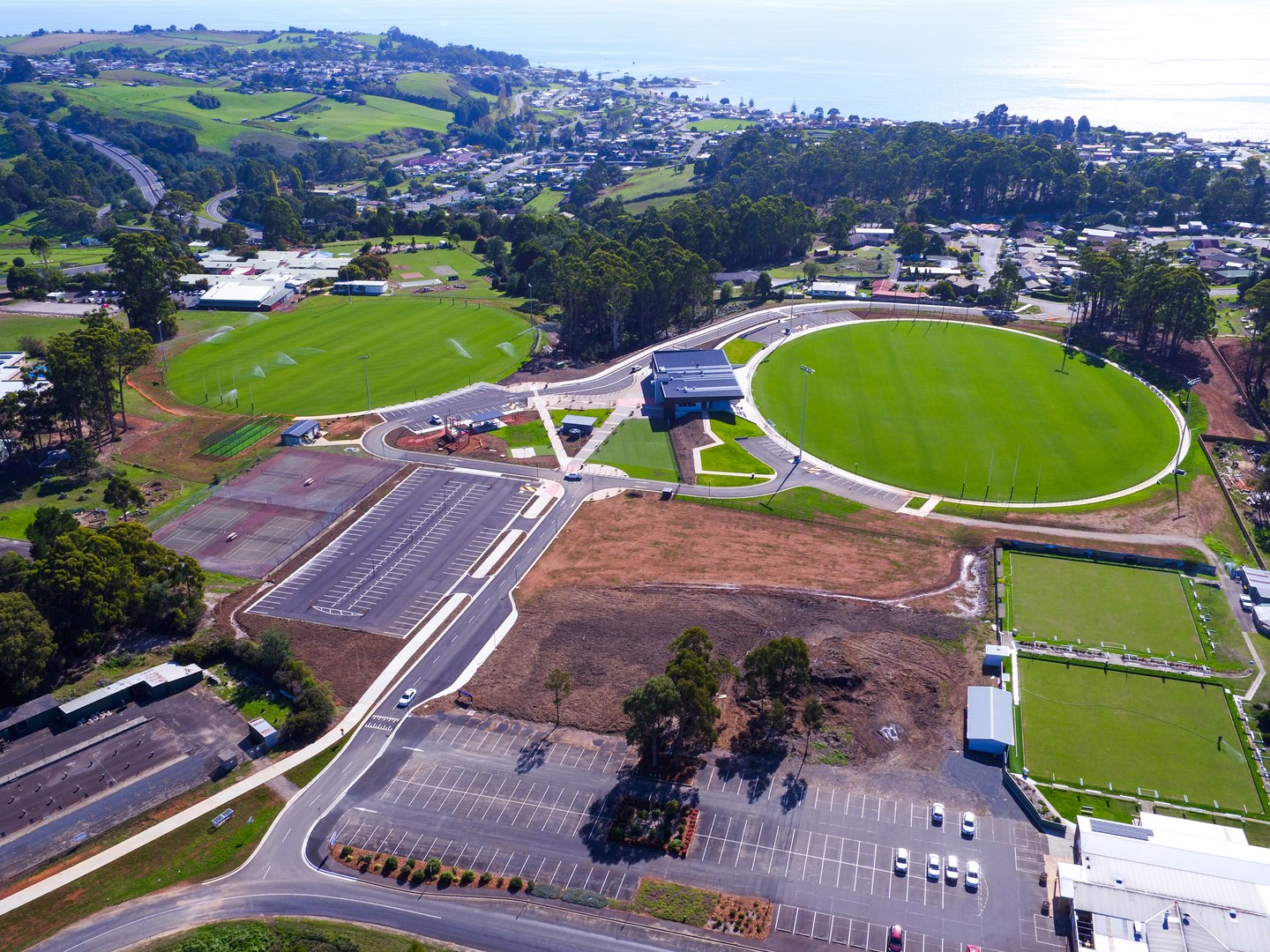 Aerial view of Dial Park in Penguin, Tasmania, showing the main oval, neighbouring sports fields, car parks, and community facilities, with the town and coastline in the background.